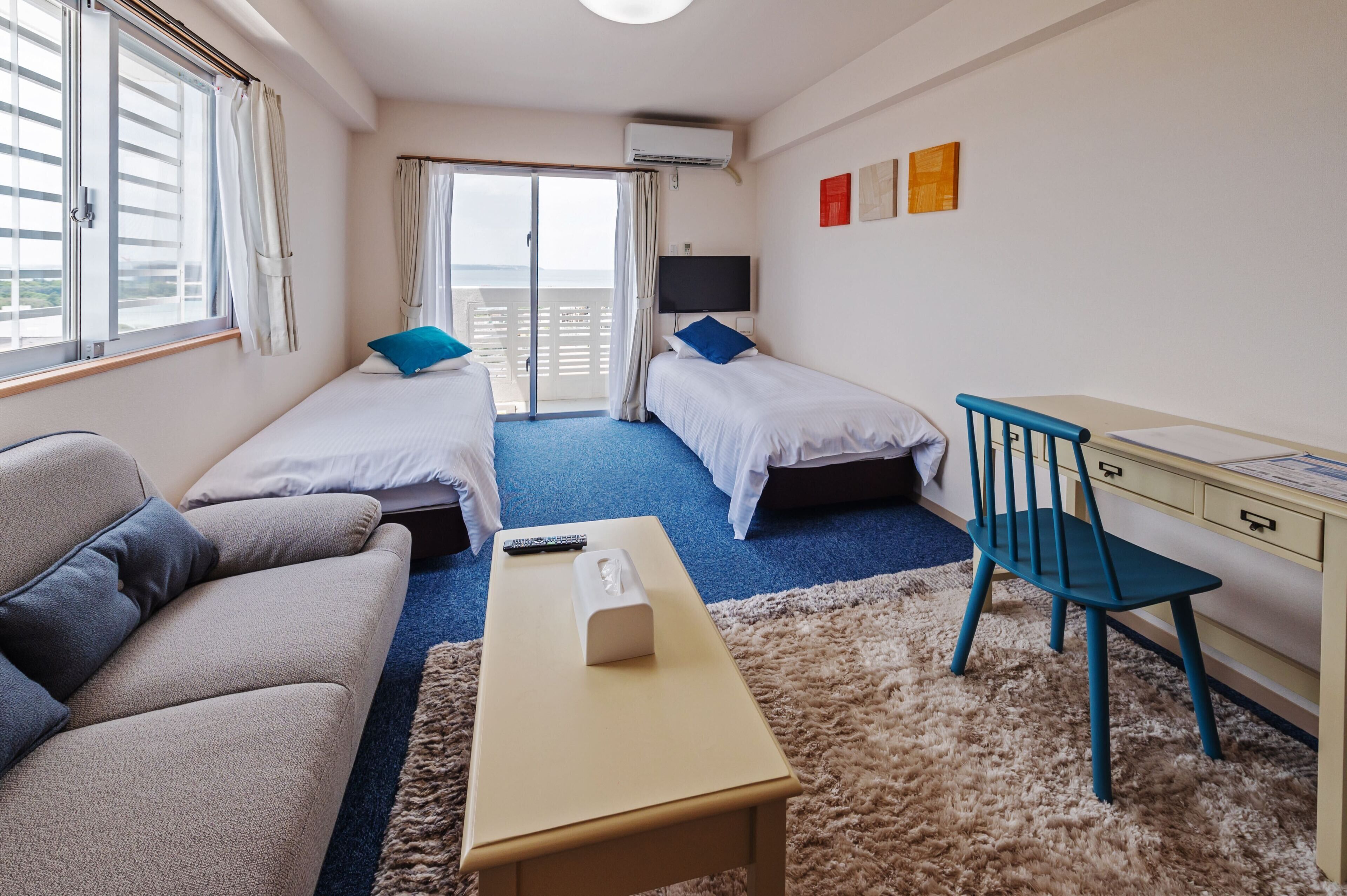 A hotel room with two beds, a sofa, a desk, and a TV.