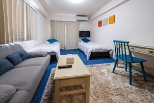Habitación de hotel con sofá, dos camas individuales, escritorio con silla, televisor y alfombra mullida.