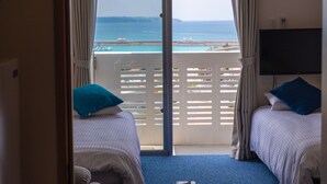 A room with two beds, a TV, and a balcony with a view of the sea. - Crystal Court (Miyakojima)