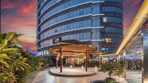 A modern hotel with a curved facade, a covered outdoor area with plants, and a sign in a foreign language. - Ronzou International Hotel (Rong County)