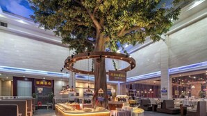 A modern hotel lobby with a central wooden reception desk, seating areas, and a large tree. - Ronzou International Hotel (Rong County)