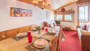 Un comedor acogedor con techo de madera, una araña, un cuadro y una ventana con cortinas.