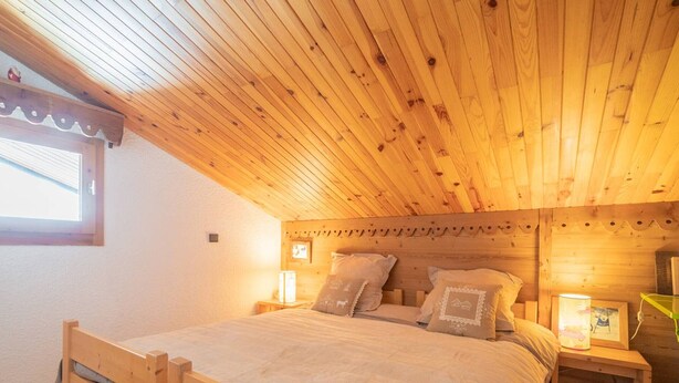Un dormitorio acogedor con techo de madera, una cama individual, dos mesitas de noche con lámparas y una ventana con cortinas.