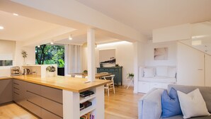 Et moderne køkken med træbordplade, et spiseområde med bord og stole, en grå sofa med hynder, og en trappe til et andet niveau.