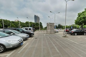 Um estacionamento com carros, um edifício alto ao fundo e árvores.
