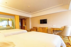 Ein Hotelzimmer mit zwei Betten, einem Schreibtisch, einem Sessel, einem Fernseher und einem Fenster mit Jalousien.