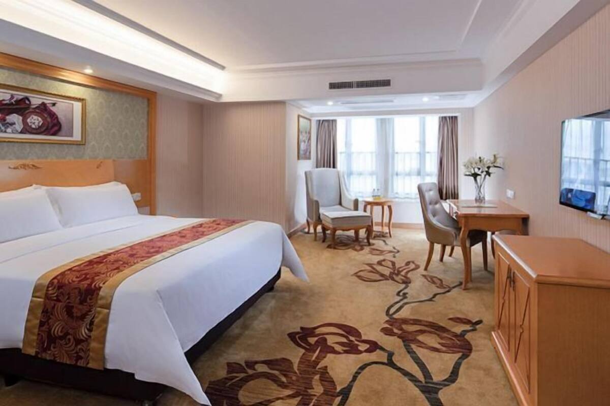 A hotel room with a large bed, a desk, a chair, and a television.