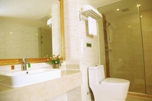 A bathroom with a sink, mirror, toilet, and glass shower enclosure. - Vienna International Hotel (Zhongshan)