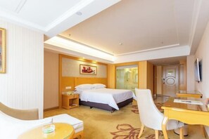 A hotel room with a bed, bedside table, chair, desk, and a television on the wall. - Vienna International Hotel (Zhongshan)
