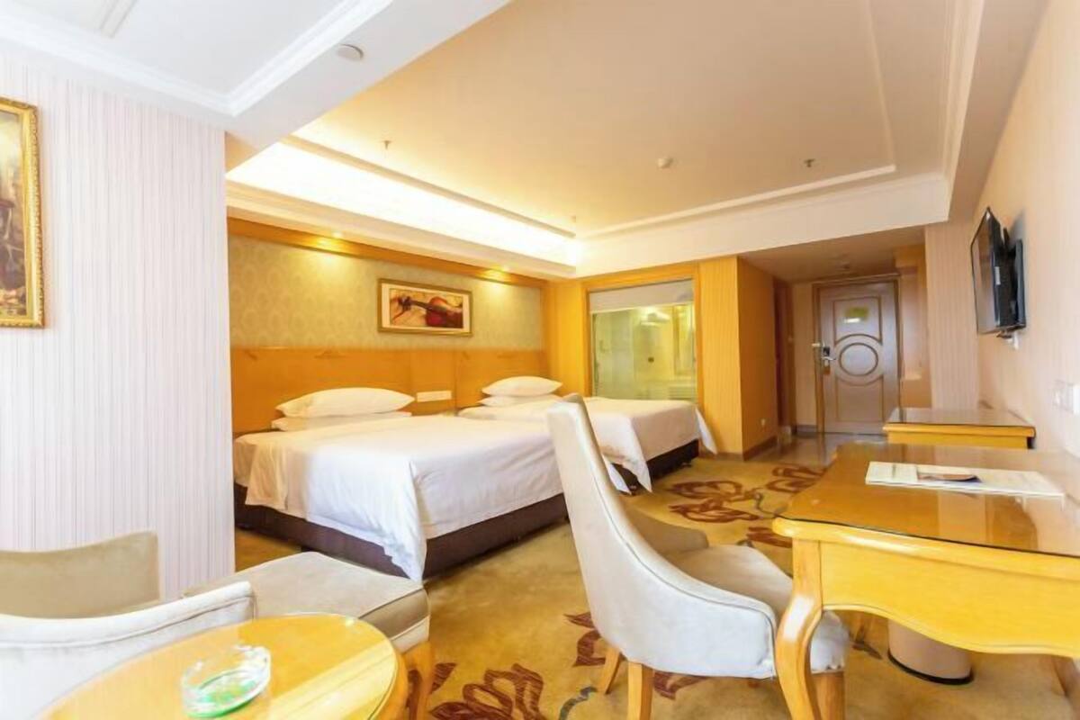 A hotel room with a bed, two bedside tables, a desk, a chair, and a television.