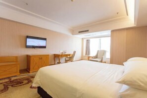 A hotel room with a large bed, a TV mounted on the wall, a desk with a chair, and a window with curtains. - Vienna International Hotel (Zhongshan)