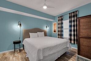Relax in this serene bedroom with a large bed and ceiling fan, accompanied by a nightstand and window with blinds.