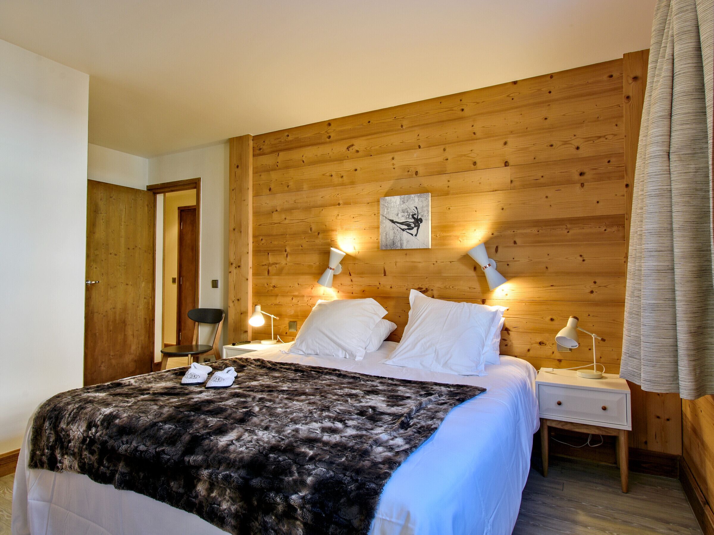 A bedroom with a wooden headboard, a bed with white linens, two bedside lamps, and a framed picture on the wall.