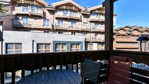 Un balcon en bois, agrémenté d’une table et de chaises, qui offre une vue sur un immeuble doté de nombreux balcons et d’une façade en pierre.
