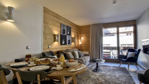Un salon moderne avec un mur en bois, un coin repas avec une table mise pour le petit-déjeuner et un balcon agrémenté de mobilier d’extérieur.