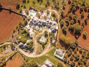 Vista aérea de um terreno com vários edifícios, incluindo uma estrutura central grande com piscina, cercada por edifícios menores e uma área ajardinada com cercas.