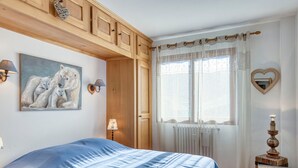 Un dormitorio con una cama grande, paneles de madera, un cuadro de osos polares, una ventana con cortinas traslúcidas y un espejo con forma de corazón.