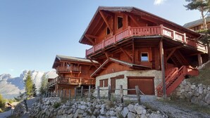 A wooden chalet with multiple balconies and a stone foundation, set against a mountainous backdrop. - Spacious chalet 14 pers., fireplace, parking La Joue du Loup (La Joue du Loup)