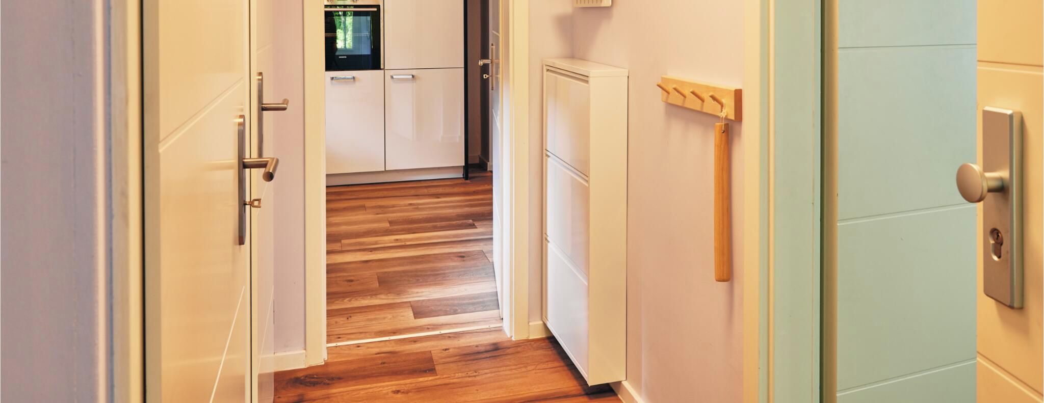 Un couloir avec un plancher en bois, un réfrigérateur blanc et une porte sur laquelle est accroché un porte-manteau.