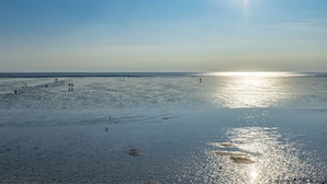 A beach with people walking and standing in the sand, and the sun is low on the horizon. - Spacious vacation apartment in a central and quiet location with terrace (Büsum)