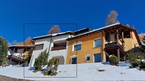 A two-story building with a balcony, a wooden staircase, and a snow-covered roof.