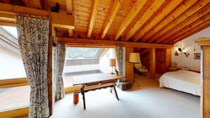 A cozy room with a wooden ceiling, a bed, a desk with a lamp, and a window with curtains.