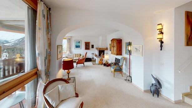 A spacious living room with a high ceiling, a fireplace, and a view of a mountain through large windows.