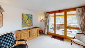 A spacious living room with a wooden cabinet, a black leather chair, a white sofa, and a large window with a view of a balcony.
