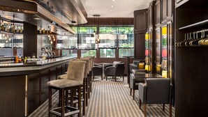 A bar area with stools, a bar counter, and shelves with bottles. There are tables and chairs in the dining area. - Amedia Siegen, Trademark Collection by Wyndham (Siegen)