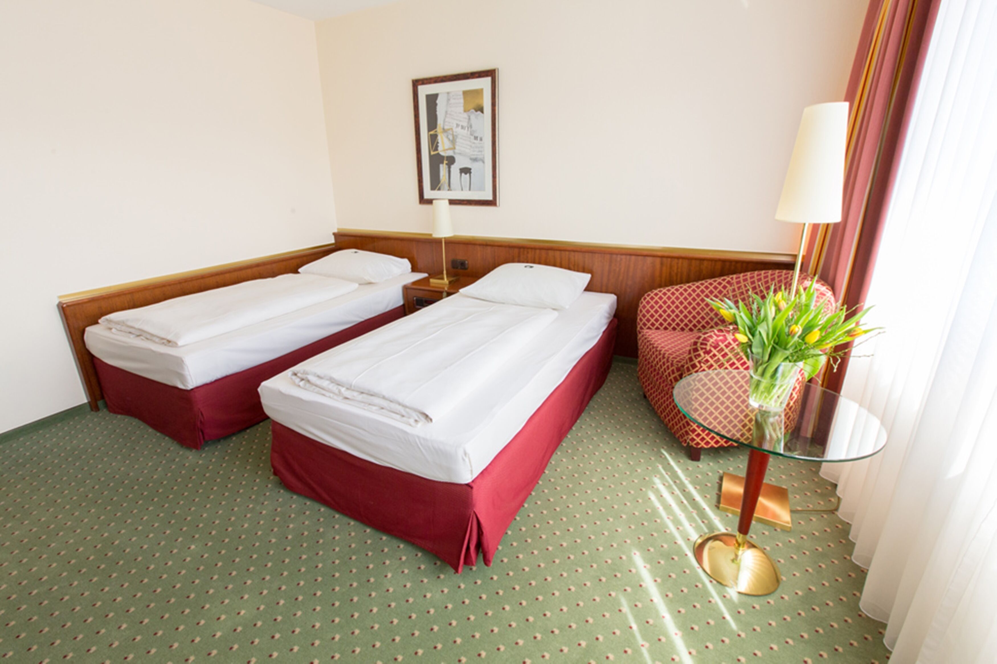 Una habitación de hotel con dos camas individuales, una mesita con un florero y un sillón estampado.