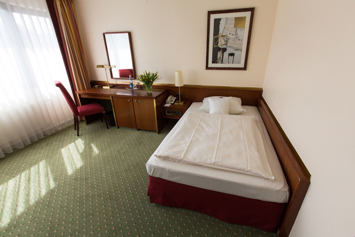 A hotel room with a bed, desk, chair, and a telephone.