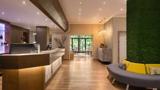 A modern reception area with a wooden reception desk, a green wall, and a seating area with a sofa and armchairs. - Amedia Siegen, Trademark Collection by Wyndham (Siegen)