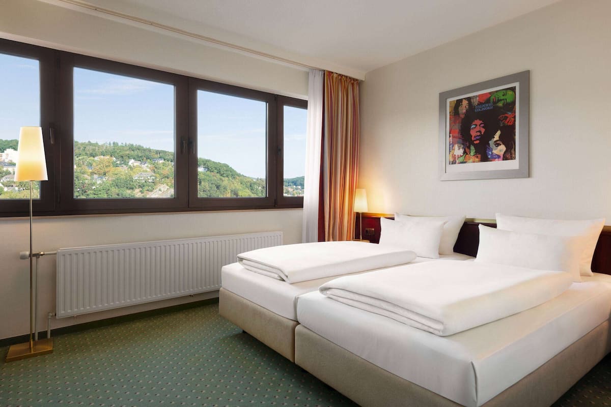 Habitación de hotel con dos camas, una ventana con vistas, un radiador y un cuadro enmarcado en la pared.
