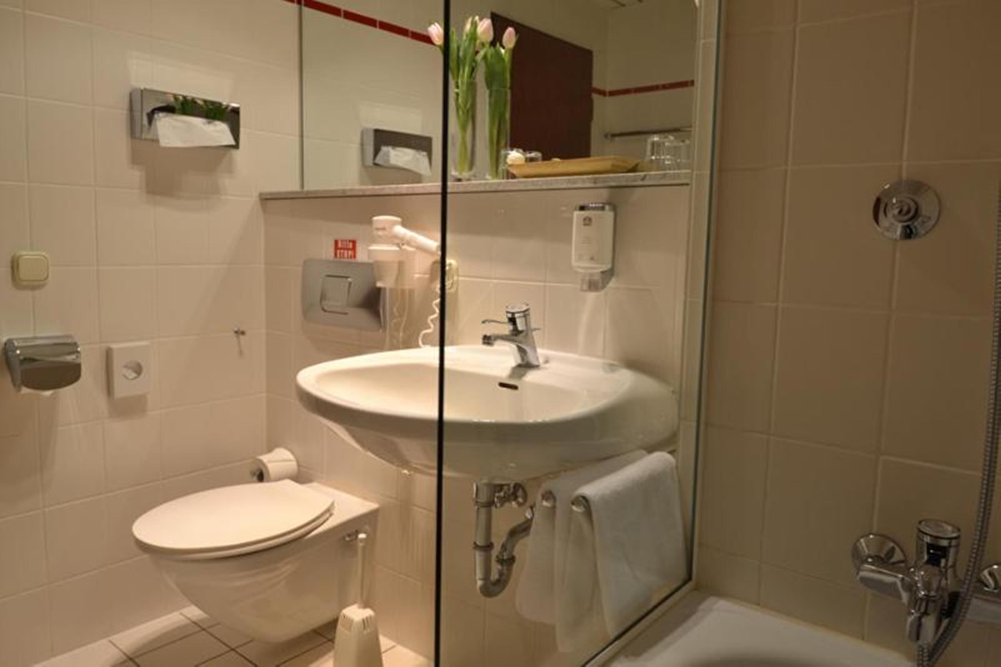Et moderne badeværelse med et glasafskærmet håndvask, toilet og brusebad.