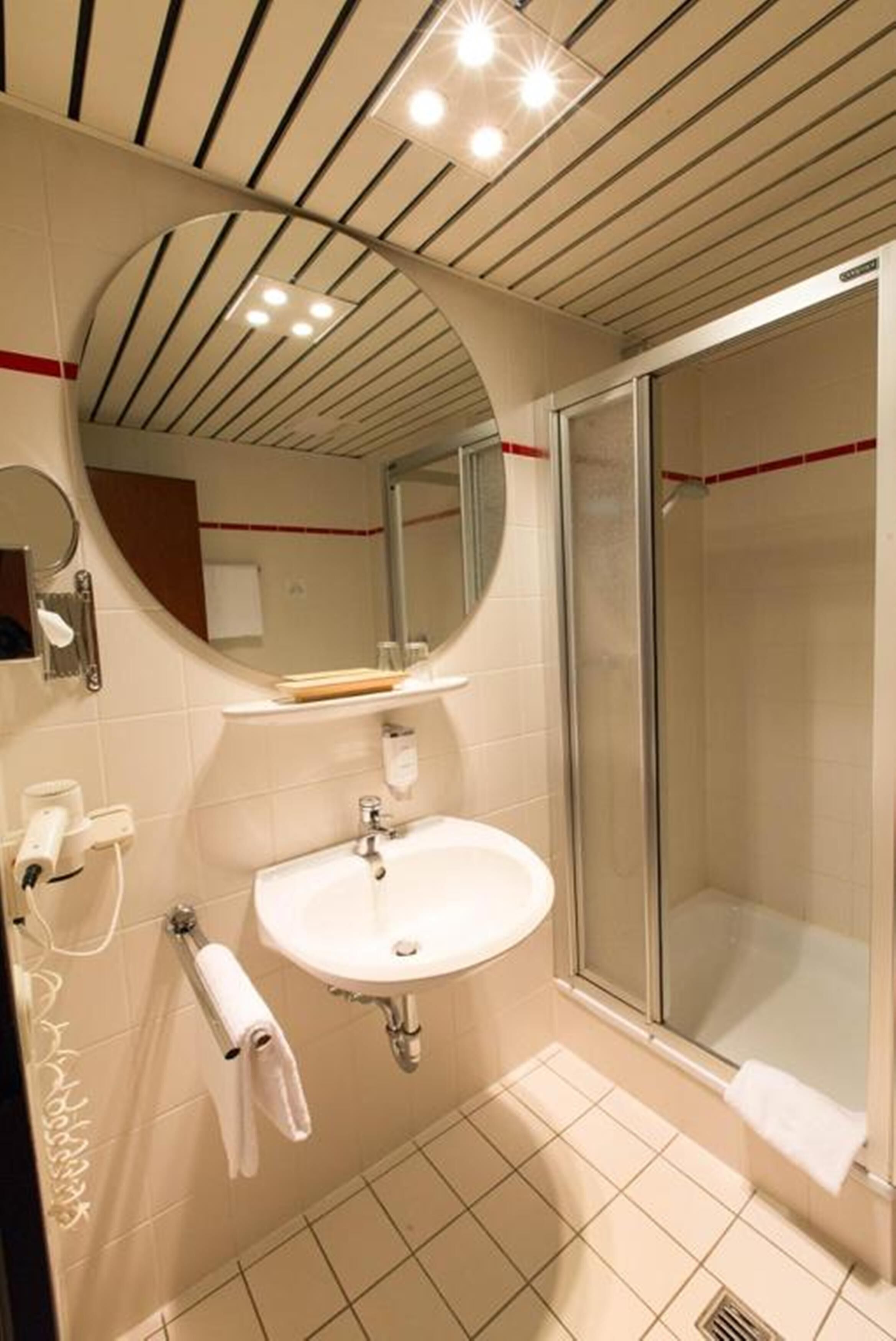 Un baño moderno con lavamanos blanco, espejo y cabina de ducha de vidrio.