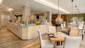 A modern hotel lobby with a central island counter, seating area, and a dining space. - Amedia Siegen, Trademark Collection by Wyndham (Siegen)