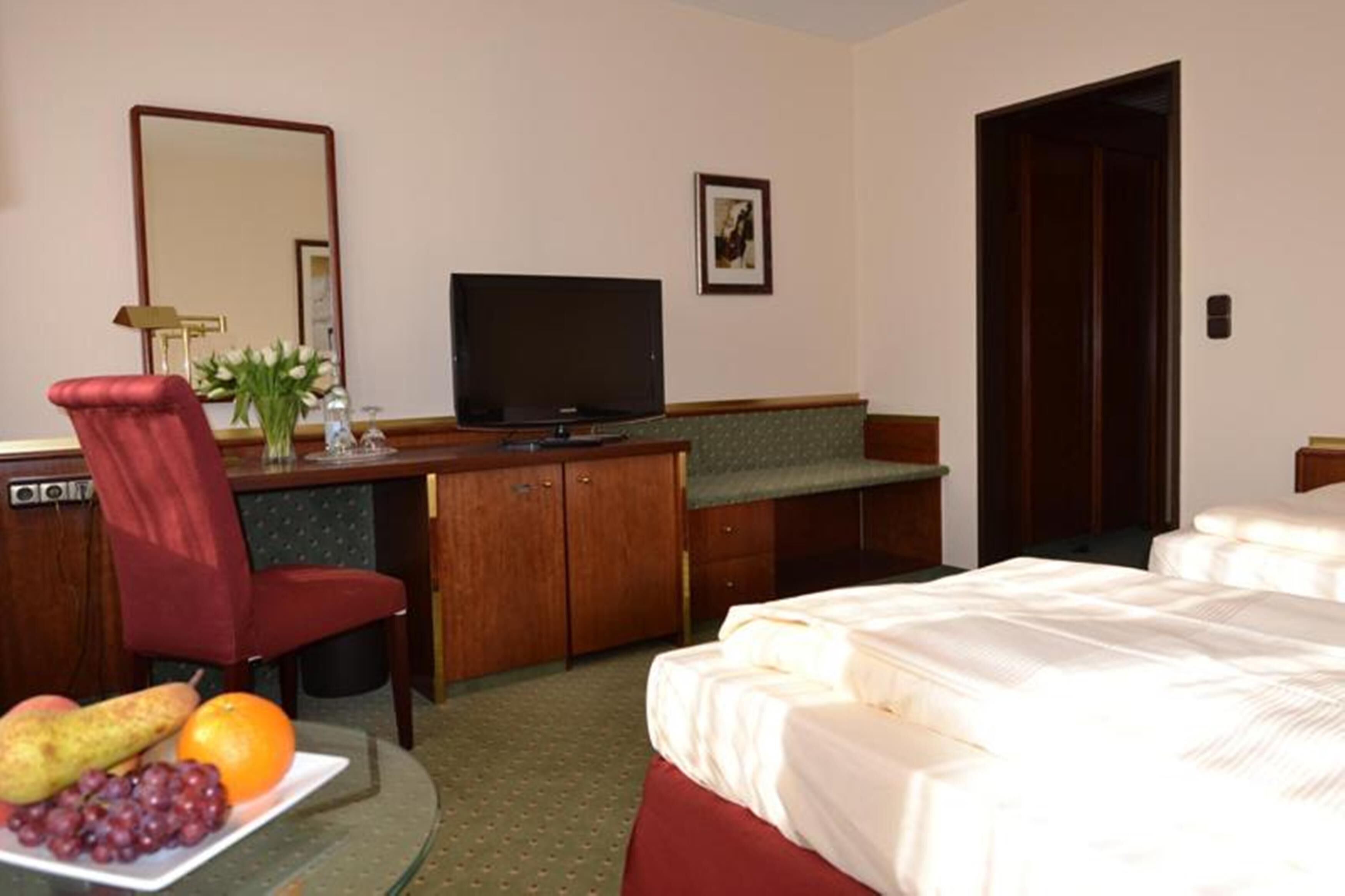 Una camera d'albergo con un letto, una scrivania con televisore, una sedia e un piatto di frutta.