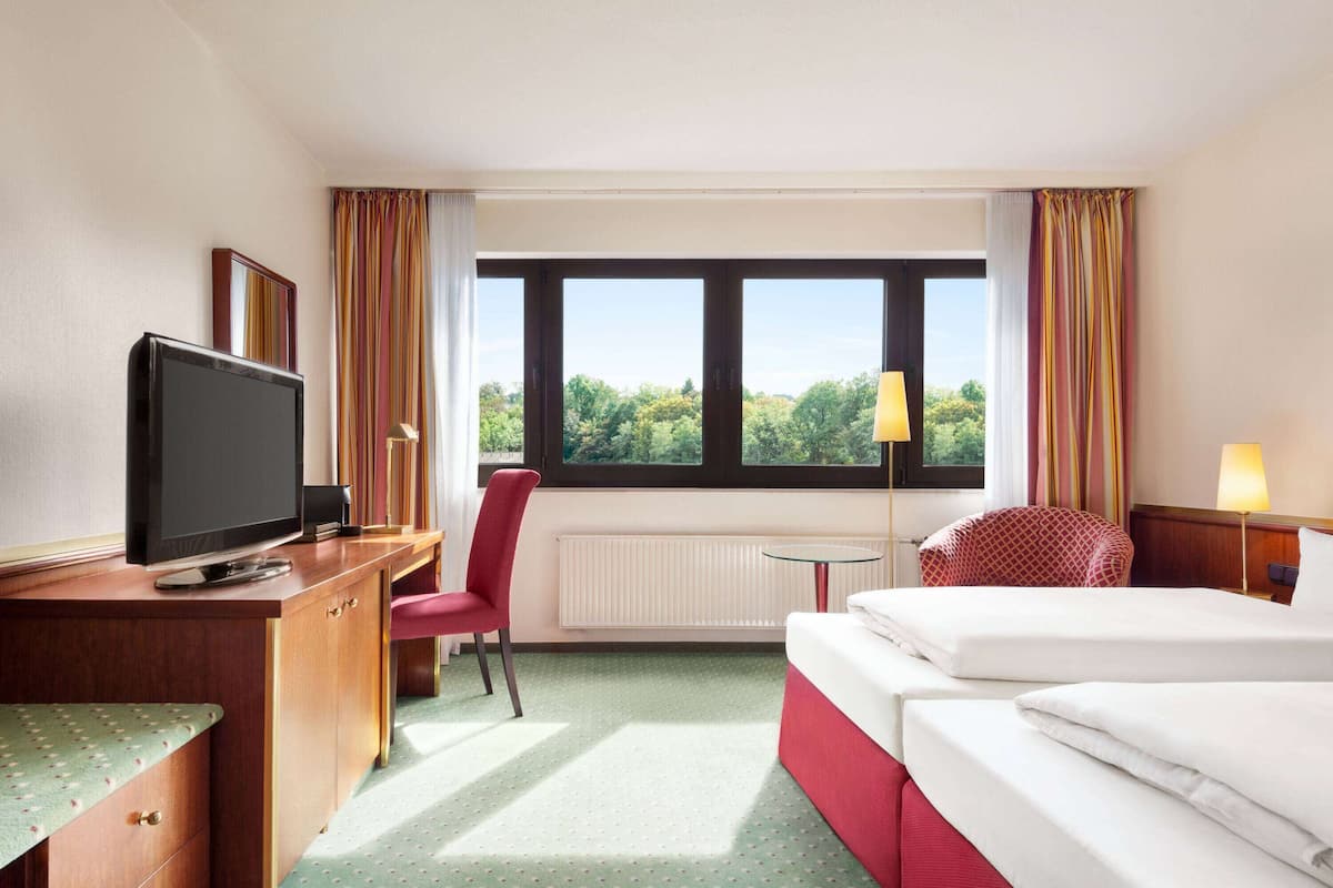 Habitación de hotel con cama, escritorio con televisor, silla, mesita y ventana con cortinas.