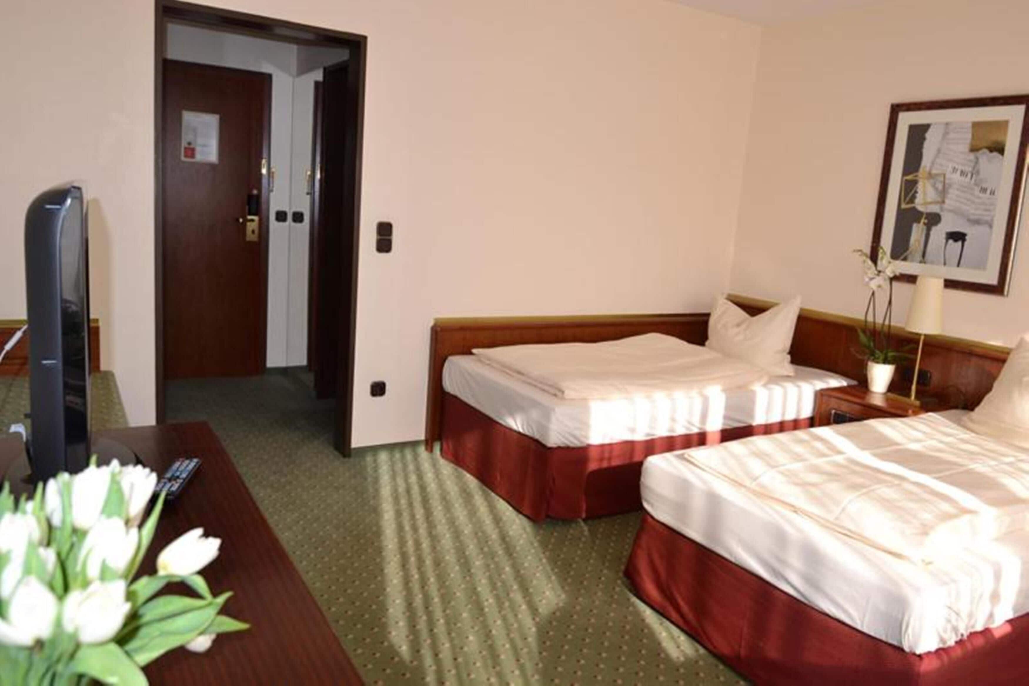 Quarto de hotel com duas camas, uma secretária com televisão e uma porta que dá para outro espaço.