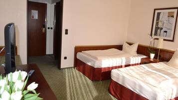 Quarto de hotel com duas camas, uma secretária com televisão e uma porta que dá para outro espaço.