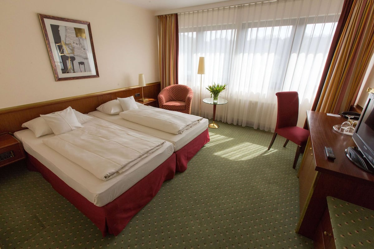 Habitación de hotel con dos camas, un escritorio, una silla, una lámpara y una ventana con cortinas.