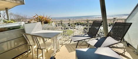 A balcony with a table and chairs, overlooking a beach.