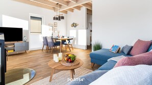 Una sala de estar moderna con un sofá, una mesa de centro con fruta, un televisor y un comedor con sillas y una mesa.