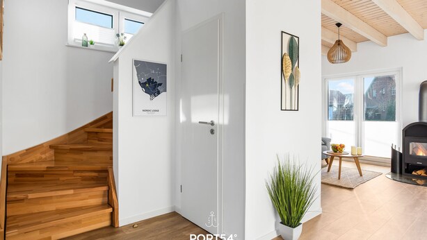 Un interior moderno con una escalera de madera, una puerta blanca, un mapa enmarcado, una chimenea y un ventanal grande.