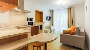 A modern kitchen with a central island, a dining area with a table and chairs, and a living area with a sofa and a flat-screen TV. - Apartamenty Swinoujscie - Villa Teresa (Swinoujscie)