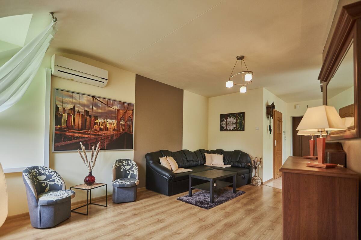 Una sala de estar moderna con un sofá de cuero negro, dos sillones, una mesa de centro y un cuadro con una vista urbana en la pared.