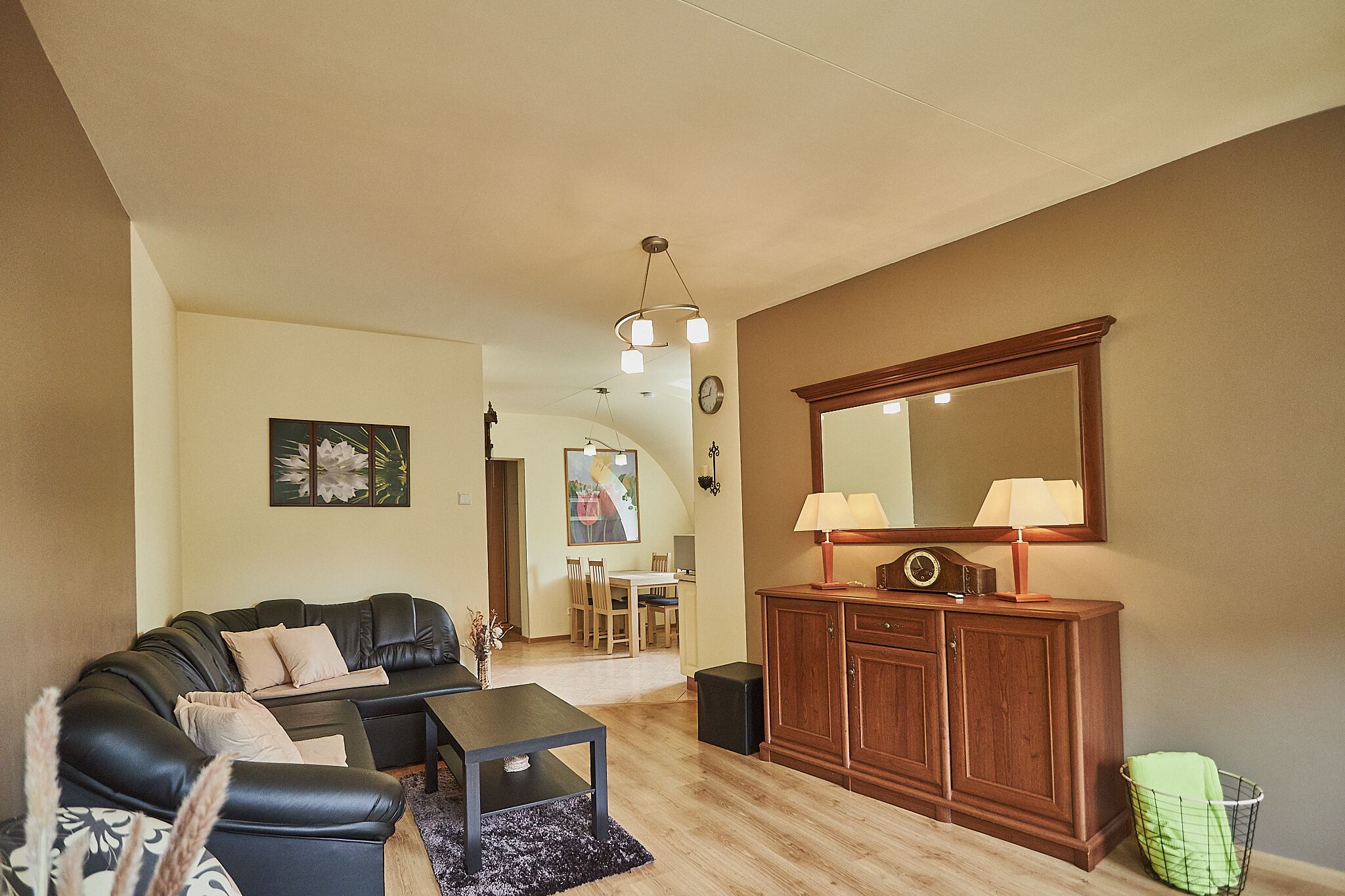 A living room with a black leather sofa, a wooden cabinet, and a dining area in the background.