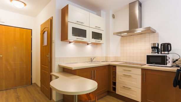 A compact kitchen with wooden cabinets, a microwave, a coffee maker, and a small bar stool. - Apartamenty Swinoujscie - Villa Teresa (Swinoujscie)