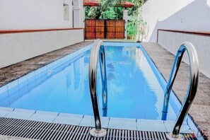 Une piscine rectangulaire dotée de barrières métalliques sur les deux côtés, entourée d’une terrasse carrelée et d’un petit muret.