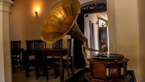 En grammofon står på ett bord i ett rum med trästolar och en väggmonterad lampa.